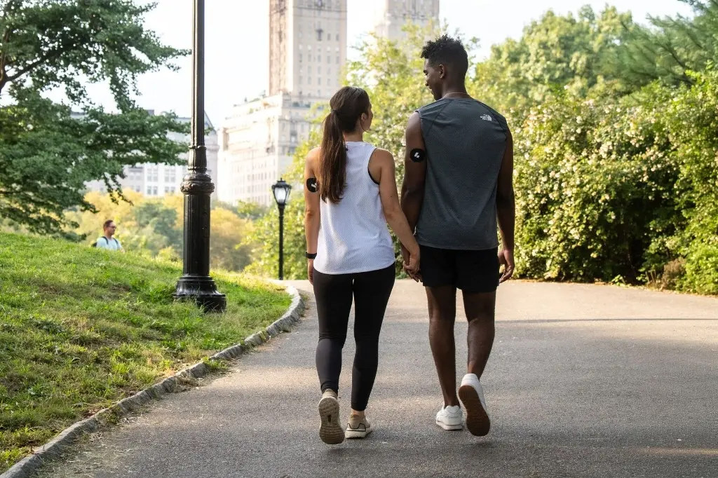 A couple walking together on a tree-lined path in a city park, illustrating the role of everyday social connection in physical health and longevity.